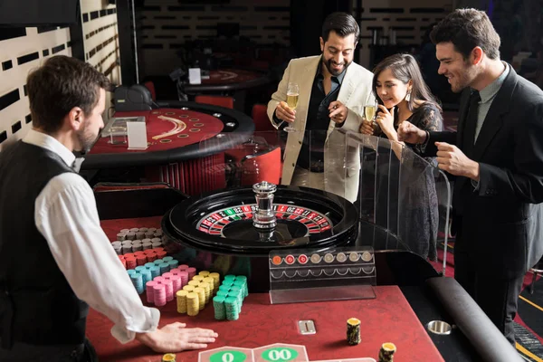 Group of roulette players placing their bets and waiting for the wheel to stop while having a good time in a casino