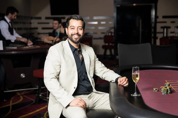 有魅力的男人穿着西装坐在赌场的扑克桌和微笑 — 图库照片