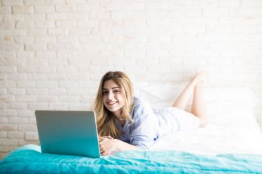 Güzel kız yatakta dizüstü bilgisayar kullanarak