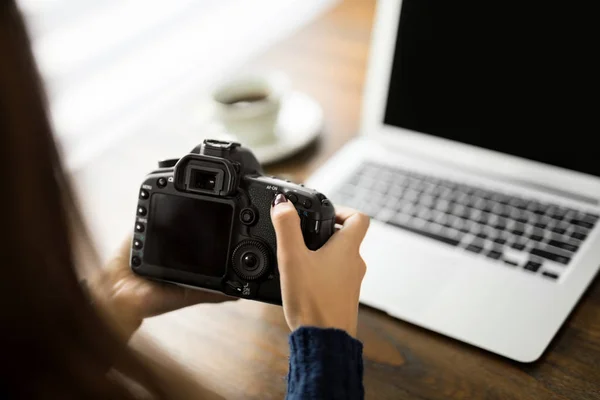 一个年轻的女摄影师持有相机和检查她的办公桌上的照片的观点 — 图库照片