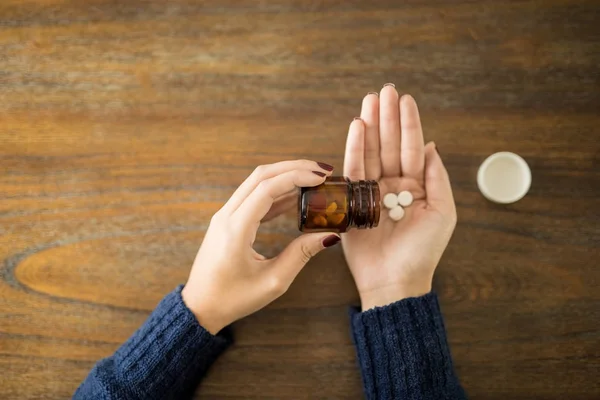 Point of view of female spilling pills onto hand over wooden table