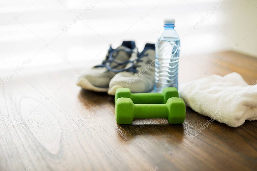 Fitness and active lifestyles concept. Dumbbells, sport shoes,  bottle of water and towel on wooden table