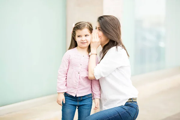 Mother telling daughter secret on storefront background