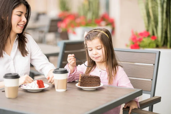女儿吃蛋糕在咖啡馆与她的母亲在模糊的背景 — 图库照片