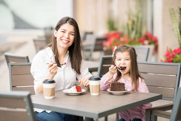 母と娘の背景をぼかした写真にカフェでケーキを食べる — ストック写真