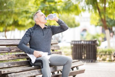 Orta yaşlı beyaz adam içme suyu bir şişe ve bir parkta çalışmasını dinlenme