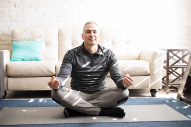 Fitness mat ve meditasyon lotus yoga poz evde oturan sağlıklı olgun adam portresi bacaklı geçti