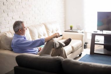 Olgun adam evde dinlenirken tv izlerken uzaktan kumanda ile oturma odasında