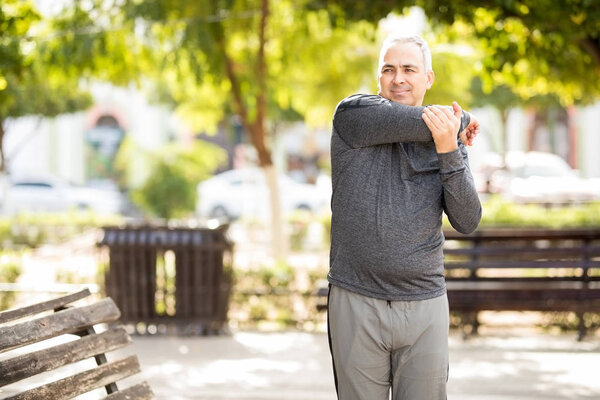 Happy mature man stretching his arms before working out in the park