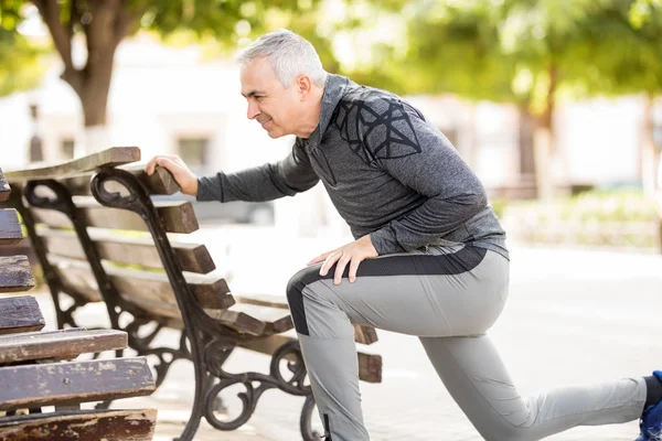 Active Latin senior man stretching on a park bench, warming up before a run.