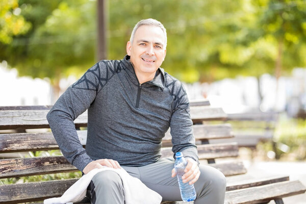 Good looking middle aged man sitting on a park bench with a water bottle after exercise session