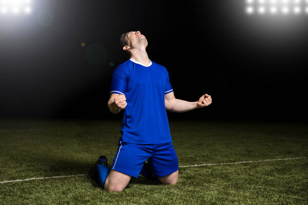Footballer sliding knees on the grass in a stadium celebrating a win