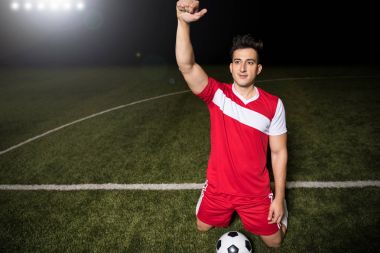 Erkek futbol oyuncusu kırmızı mayoyu gol dizlerinin üzerinde duran ve kol kaldırdı sonra heyecanlı