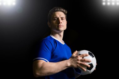 Yakışıklı genç futbolcu bir topu tutarak ve tr göz teması Stadı yapma mavi üniformalı portresi