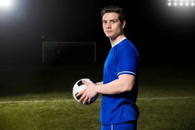 Işıklar altında sahada futbol ayakta tutan yakışıklı genç futbolcu portresi