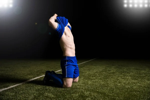 庆祝足球运动员在他的膝盖在草地上与新泽西在他的头上进球后的球 — 图库照片