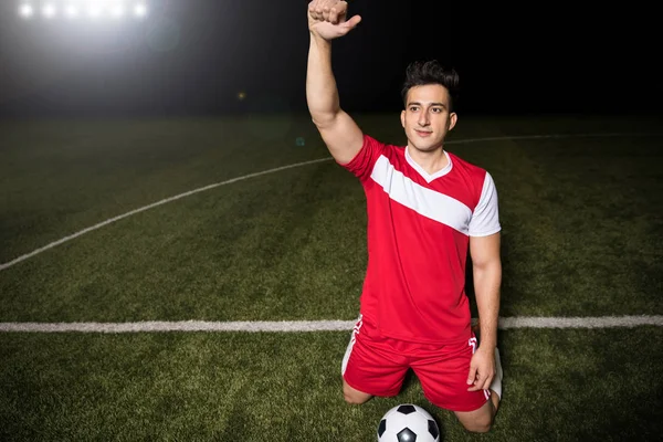 兴奋的男子足球运动员在红色球衣进球后 站在他的膝盖和手臂提出 — 图库照片