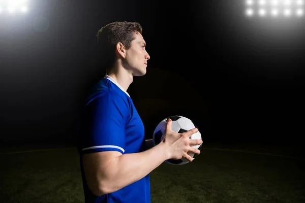 适合年轻足球运动员的外形视图蓝色球衣站在运动场上 手里拿着足球 — 图库照片