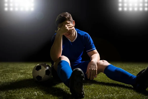失望的足球运动员在蓝色坐在球场后输了比赛 — 图库照片