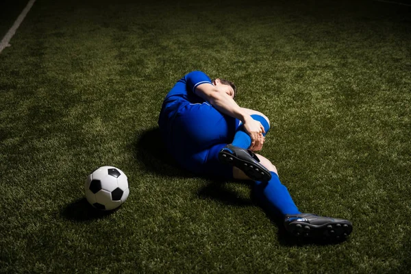 Soccer player lying down on ground with leg injury during football match