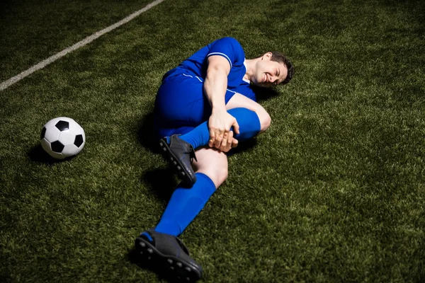 Injured soccer player lying on the ground and holding his leg during a football game