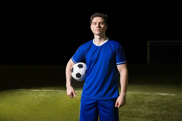 职业足球运动员的肖像穿着蓝色制服站在足球场上 他的胳膊下球 — 图库照片