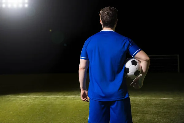 橄榄球运动员的后方看法在蓝色球衣与球在他的胳膊之下在体育场 — 图库照片