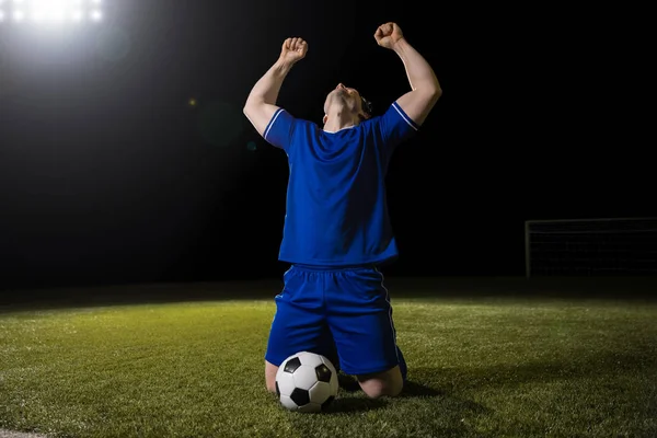 欣喜若狂的足球运动员在膝盖上举起他的手臂在体育场庆祝足球比赛胜利 — 图库照片