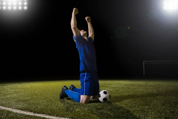 Hedef çim sahada kollarını kaldırdı diz çökmüş puanlama mavi jersey kutlayarak genç mutlu ve heyecanlı futbol oyuncusu