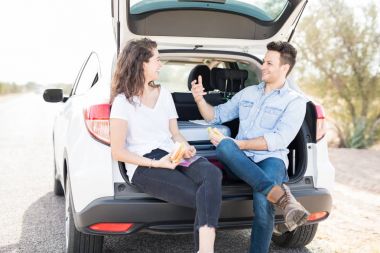 Arabanın bagajında oturan ve incelerken sandviç yemek Çift
