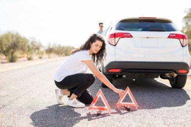 kırık araba yakınındaki yolda kırmızı acil durum durdurma üçgeni koyarak kadın işaretleri