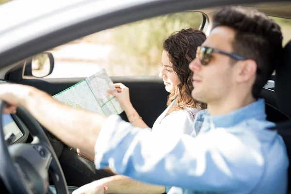 若い男が彼のガール フレンドが助手席で地図を見ている間車を運転して — ストック写真
