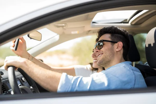 車でスマート フォンを Selfie のガール フレンドと若い男の側面図 — ストック写真