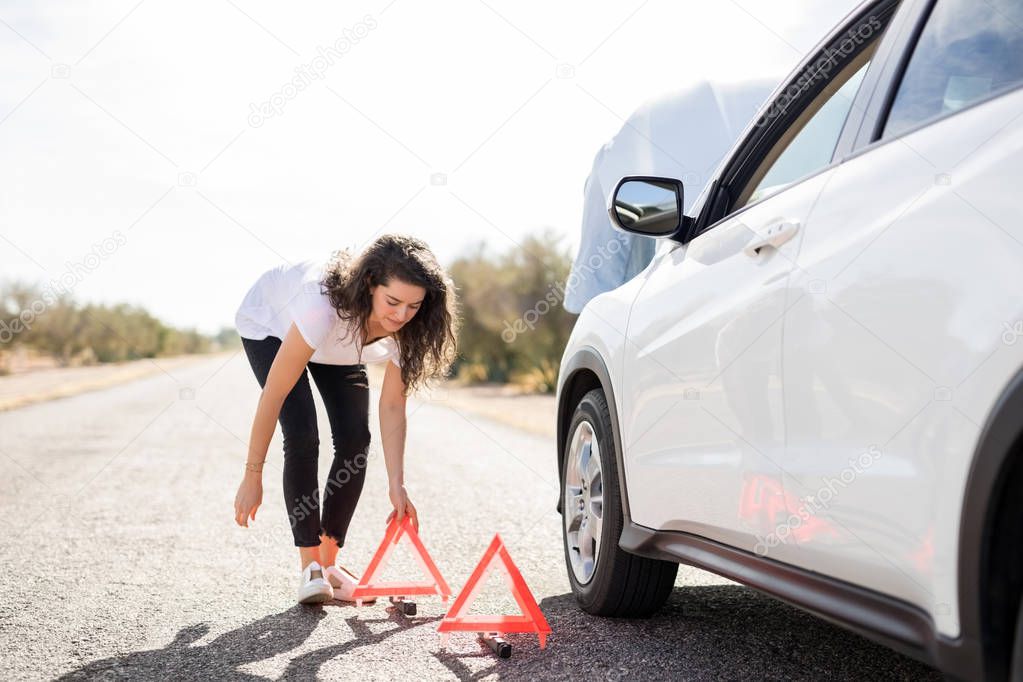 woman putting red emergency stop triangle signs on road near broken car