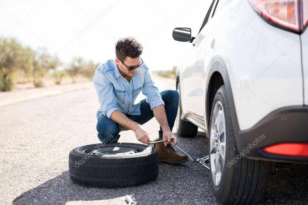 young man lifting the car on jack for changing flat tire on road
