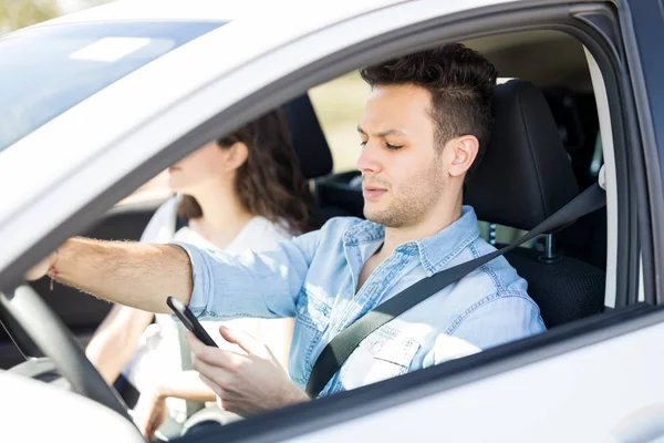 年轻男子使用智能手机 而驾驶汽车与女友 — 图库照片