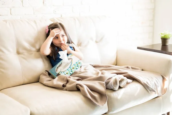客厅沙发上的小女孩抱着温度计和纸巾盒 — 图库照片