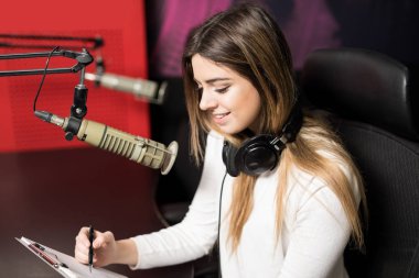 Portrait of young female radio host at radio station with headphones and microphone clipart