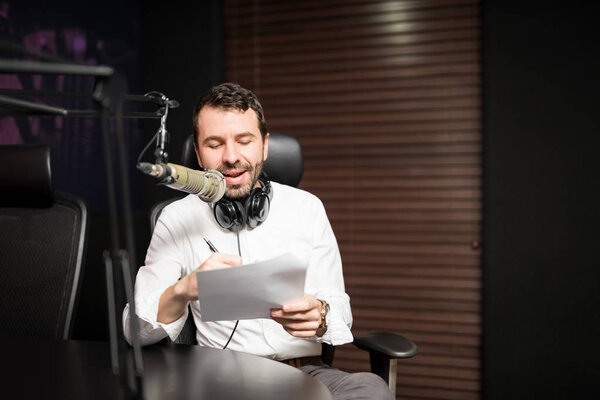 Portrait of young male radio host at radio station with headphones and microphone