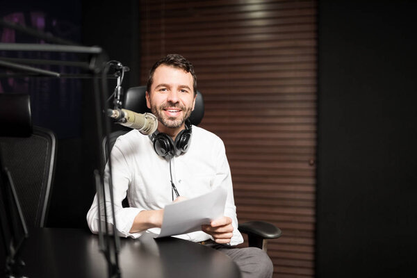 Portrait of young male radio host at radio station with headphones and microphone