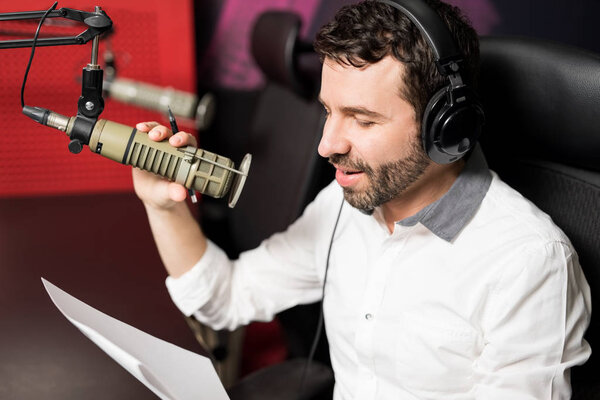 Portrait of young male radio host at radio station with headphones and microphone