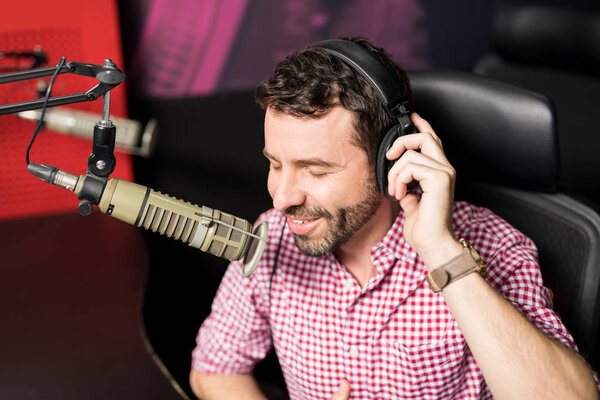 Portrait of young male radio host at radio station with headphones and microphone