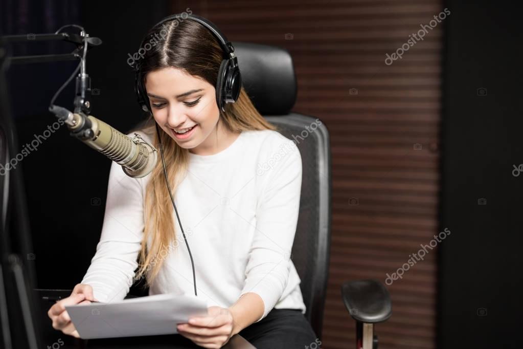 Portrait of young female radio host at radio station with headphones and microphone