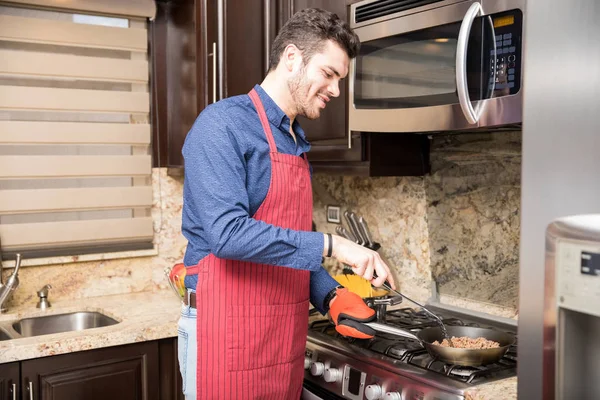 Young Hispanic man wearing an apron cooking on stove in kitchen