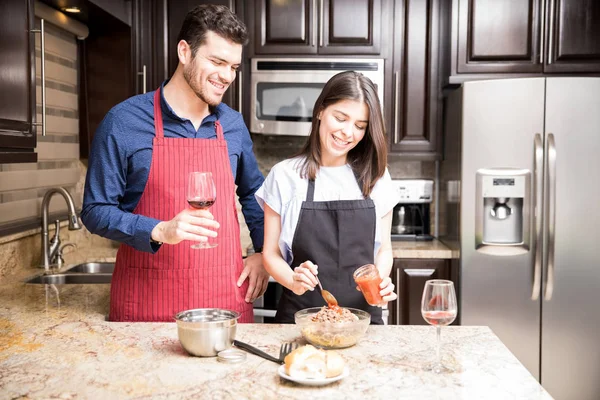 ボウルに ワインのガラスを保持している男の成分を混合エプロンで女性との台所で食糧を準備する美しい若いカップルの肖像画 — ストック写真