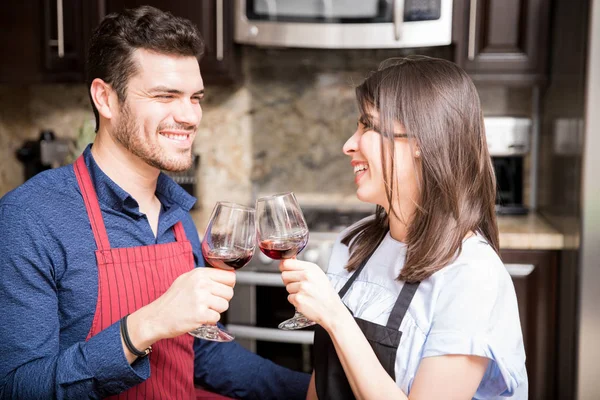 キッチンのガラスのワインを乾杯エプロンで幸せな若いカップルの肖像画 — ストック写真