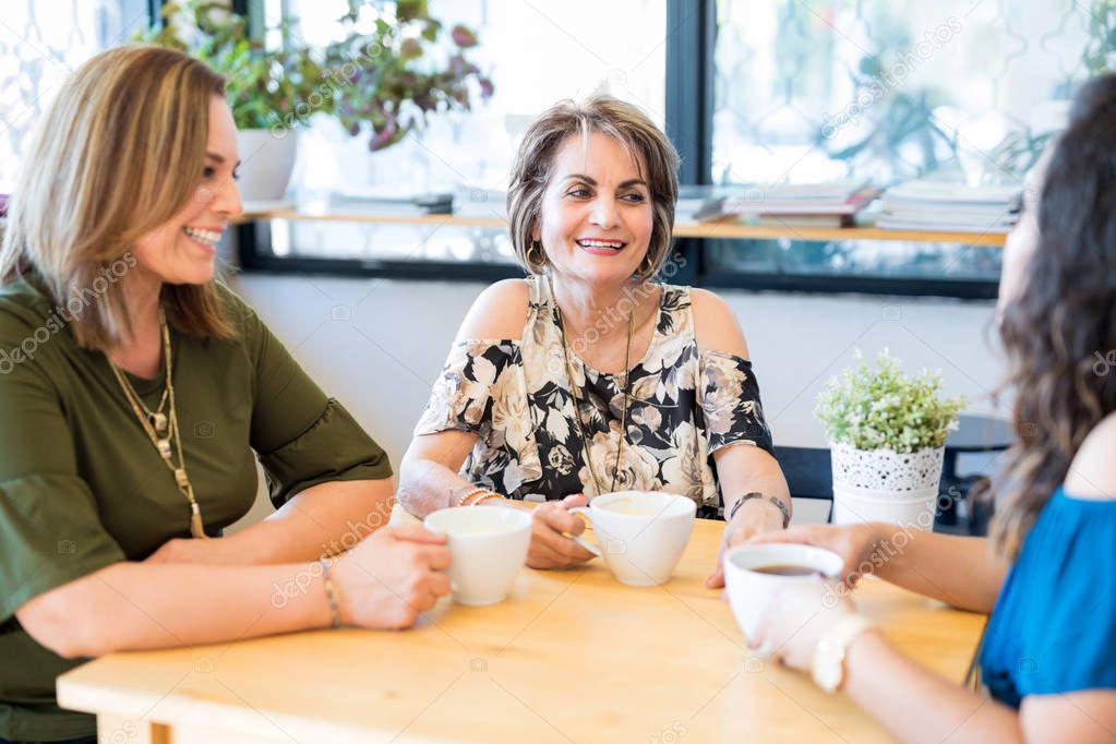 Pretty middle aged female with friends relaxing in a cafe and talking over coffee