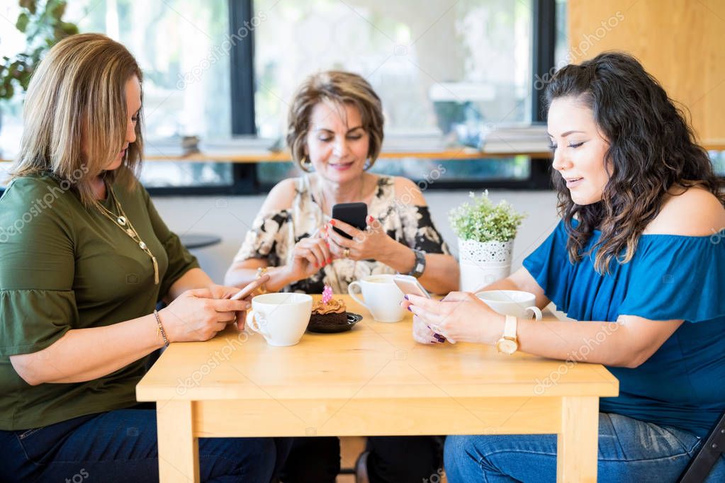 Group of three women using their own mobile phone while sitting at cafe table