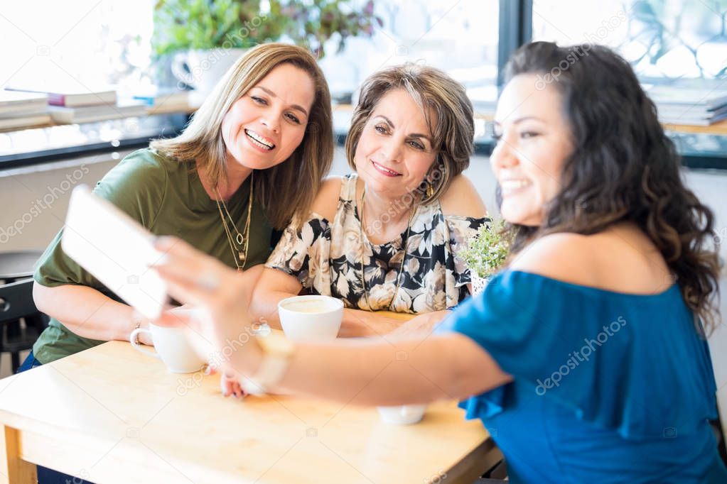 Young woman taking selfie with friends at coffee shop