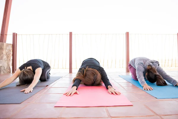 三名年轻妇女坐在瑜伽垫上 手伸着脚 在瑜伽课上伸出双手 — 图库照片